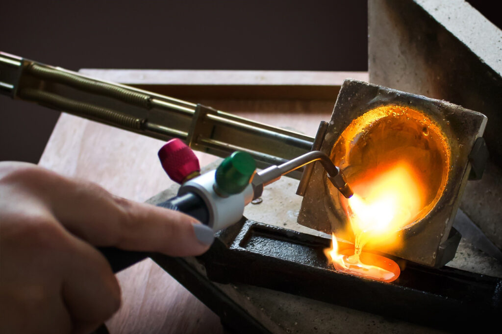 Imagem com metal derretido sendo vertido de um cadinho para uma lingoteira